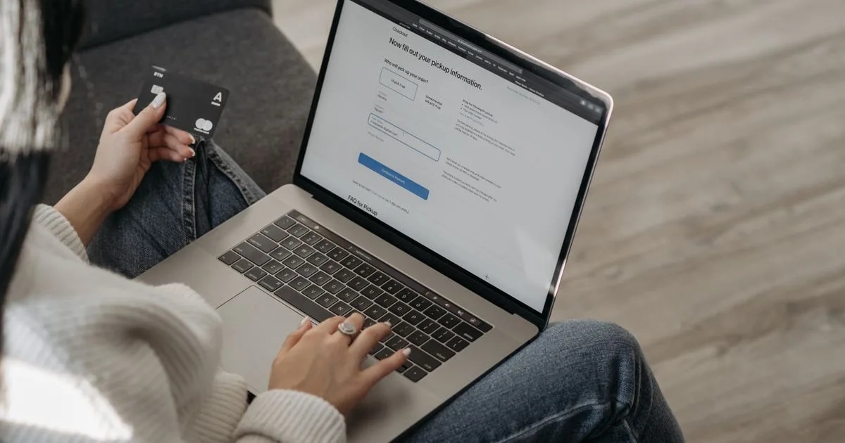 A woman using a laptop while holding a credit card, representing an online checkout moment shared by SaaS renewals and ecommerce purchases alike
