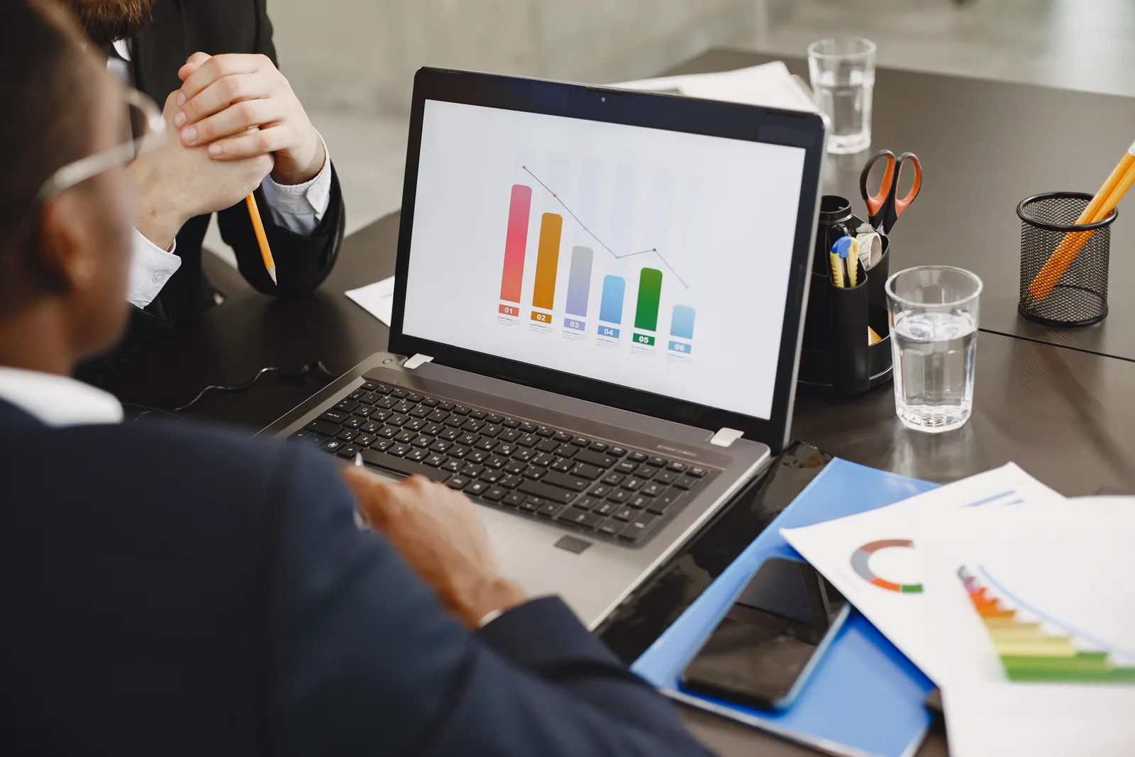 Two colleagues discussing a revenue graph on a laptop during an office meeting