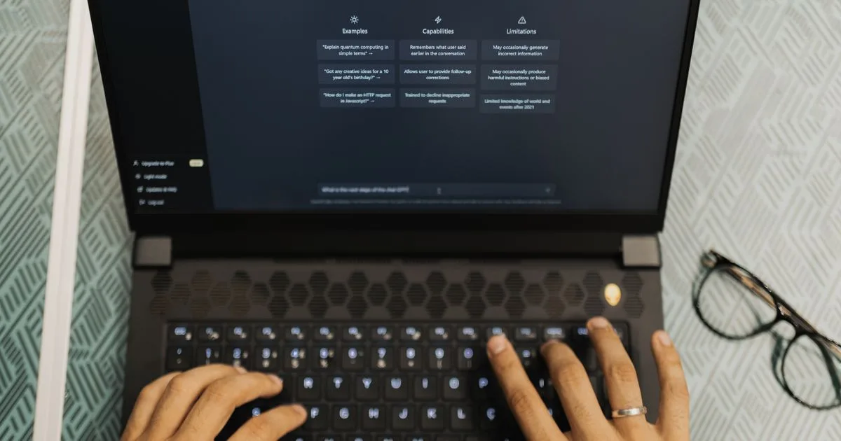 Photo of hands typing on a laptop with a ChatGPT-style AI assistant interface open