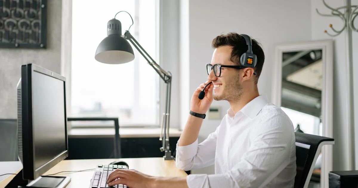 A smiling customer support representative wearing a headset while working at a computer